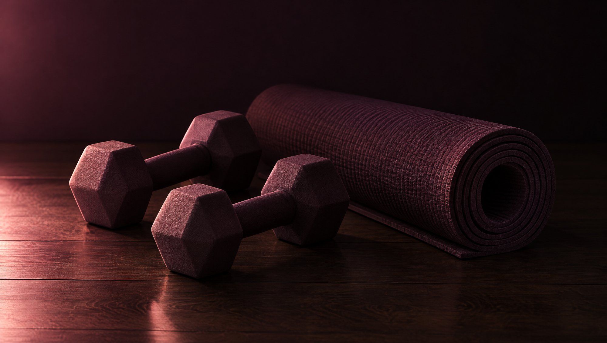 A pair of small hexagonal dumbbells and a rolled exercise mat on a dark wooden floor in rose side light.