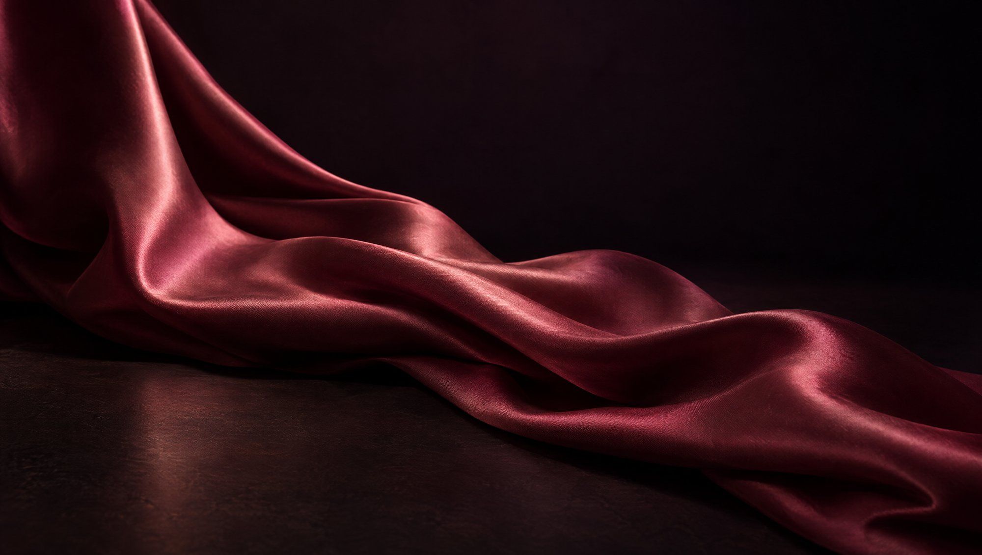 A length of deep rose silk fabric draped in soft folds across a dark surface.